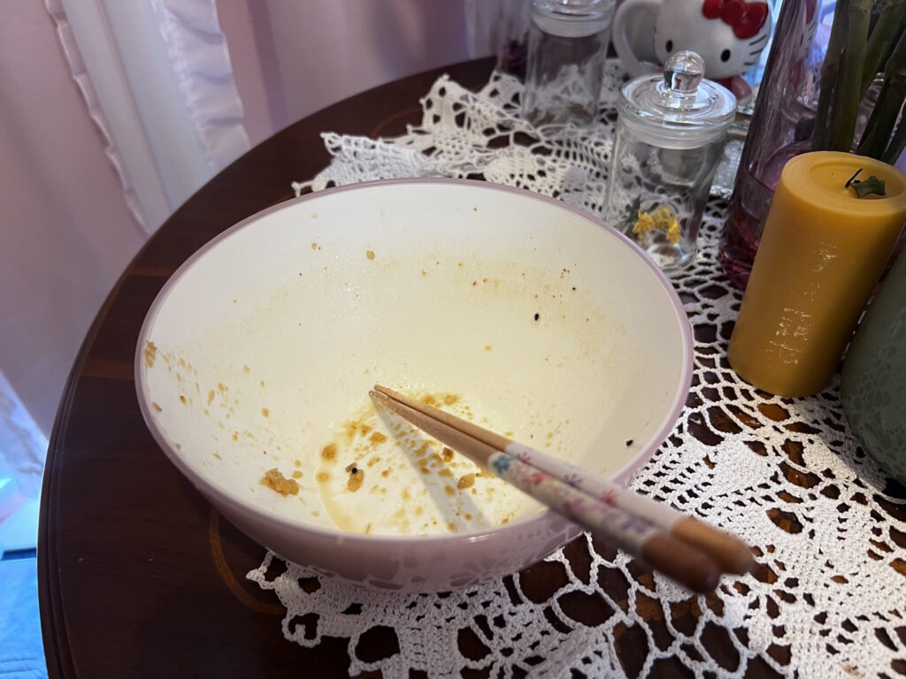 Empty pink ramen bowl with only broth residue left, chopsticks resting across it