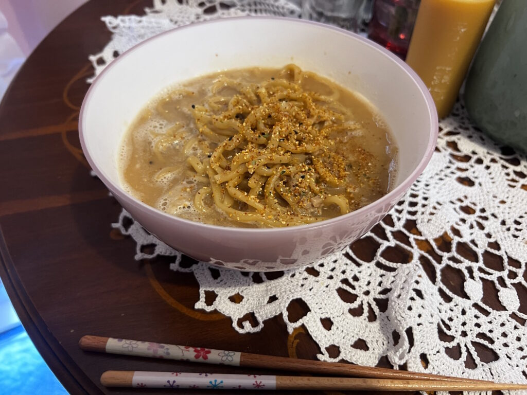 Cooked bowl of ramen topped with shichimi spice, served in a pink bowl with chopsticks