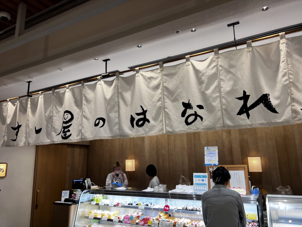 Hanare takeout counter with a large white noren curtain reading すし屋のはなれ in brushstroke calligraphy
