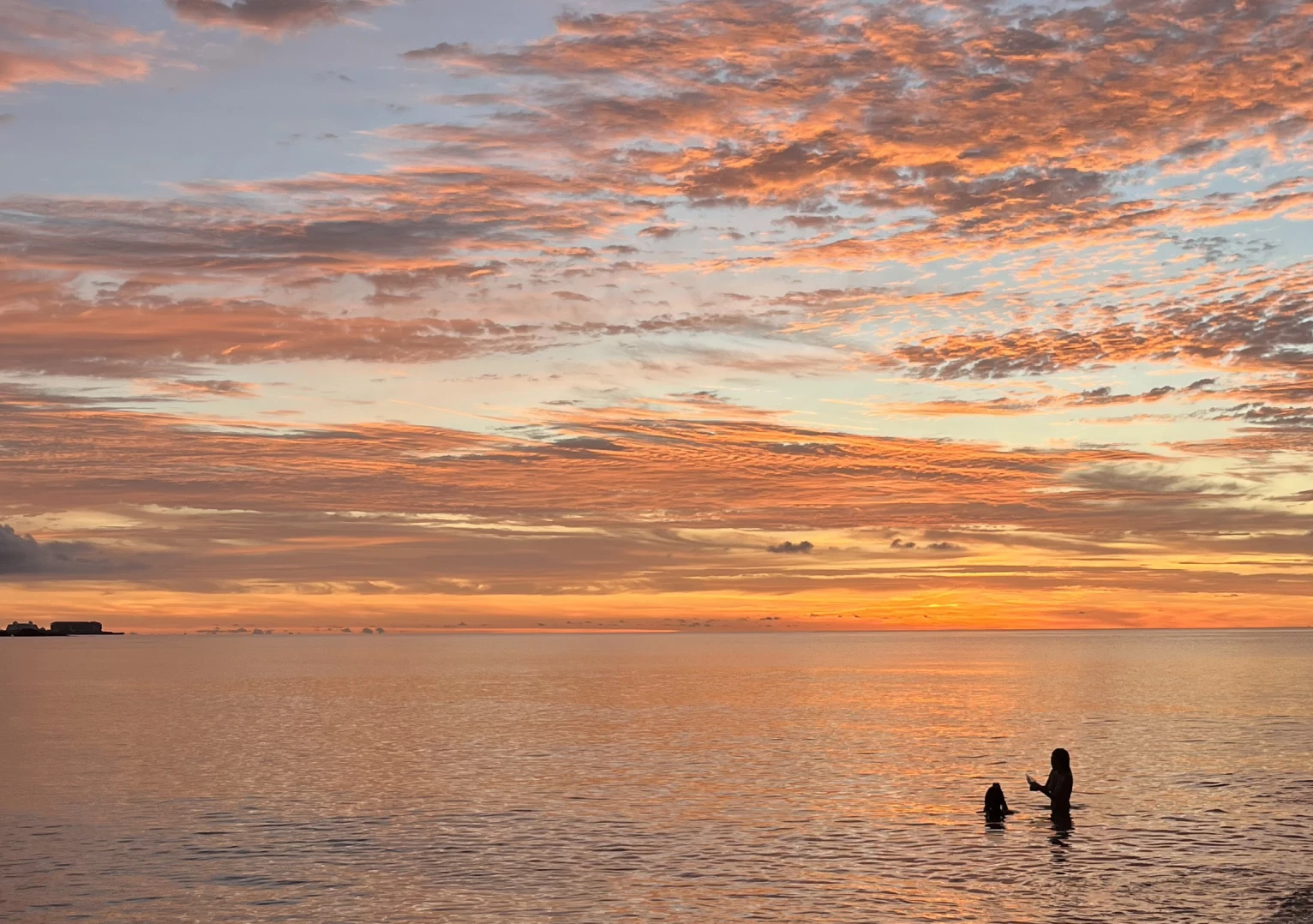 Two figures wading in calm water under a vivid orange and pink Okinawan sunset