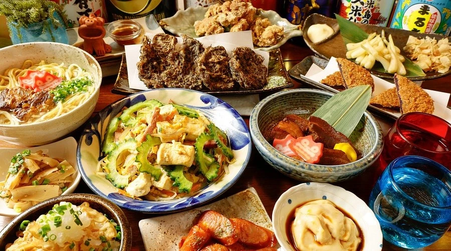 Spread of traditional Okinawan dishes including goya champuru, sashimi, and awamori
