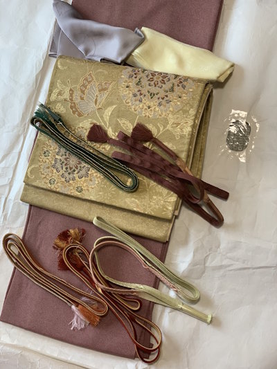 Gold brocade obi with butterfly motifs alongside obijime cords and kimono accessories laid out for styling