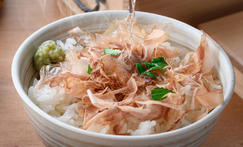 Hot broth poured over a bowl of rice topped with katsuobushi flakes and wasabi
