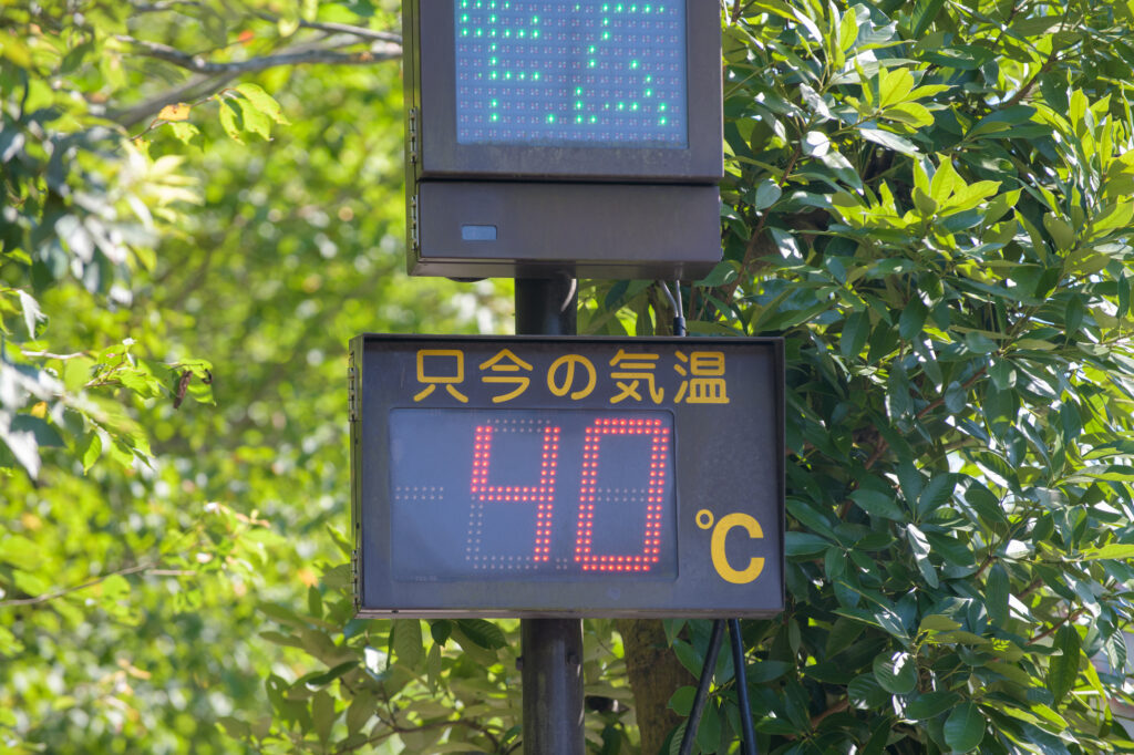 Outdoor electronic sign reading 40°C against green foliage in Japan.
