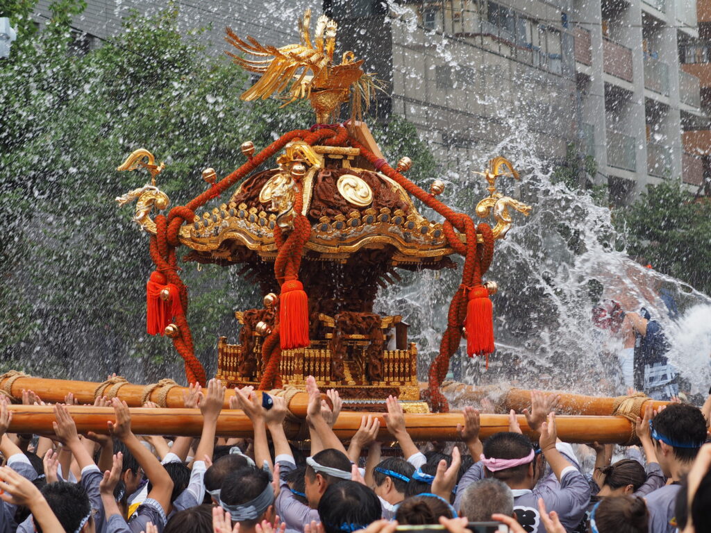 Crowds carry a gilded phoenix-topped mikoshi as water is thrown over it at the Fukagawa Hachiman festival