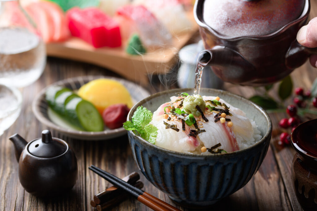 Hot broth poured from a teapot over a bowl of tai chazuke with nori and wasabi