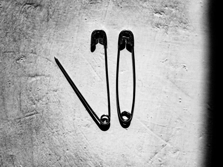 Two safety pins against a concrete wall
