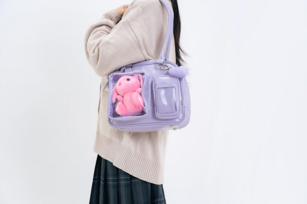 A person carries a clear-window purple bag with a small pink bunny plushie tucked inside