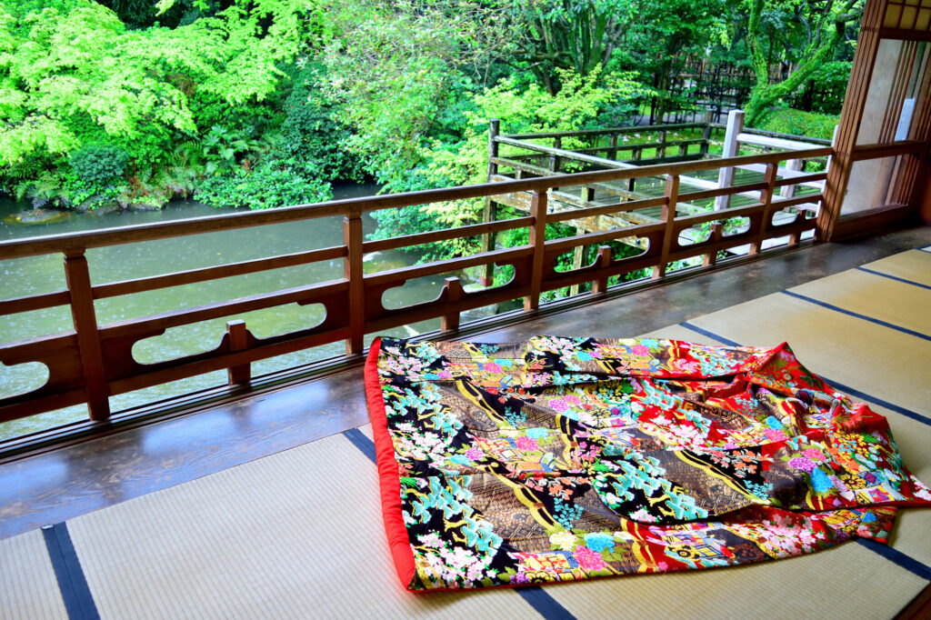 Richly embroidered uchikake robe spread on tatami overlooking a lush Japanese garden