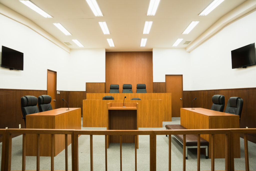 Empty Japanese courtroom with a wood-paneled judge's bench, witness stand, counsel tables, and a gallery railing