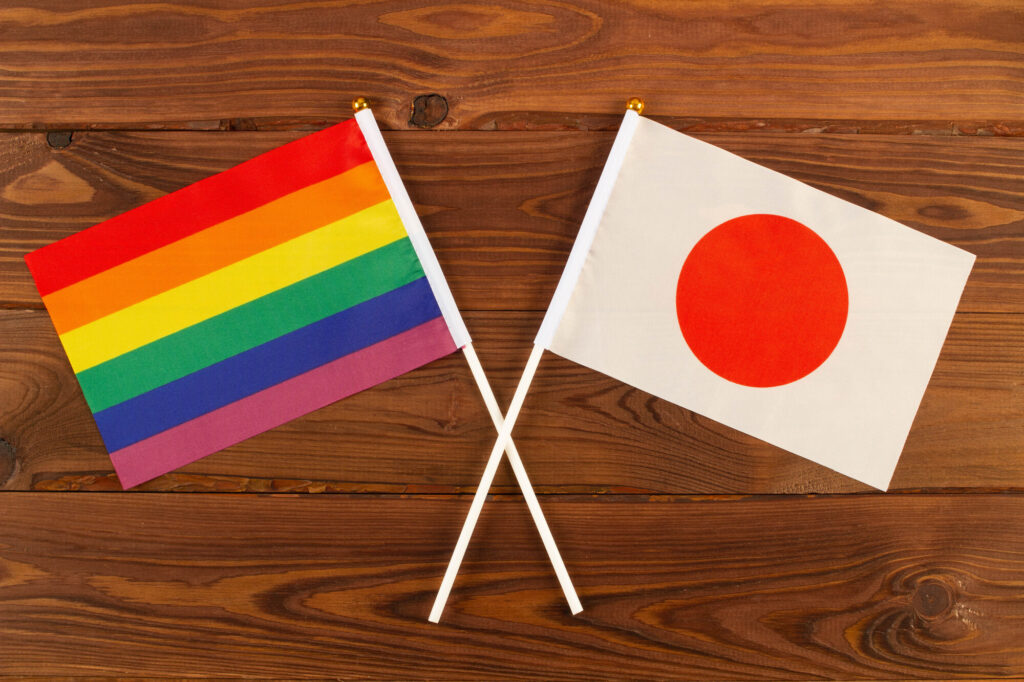 A rainbow pride flag and a Japanese flag crossed together on a wooden surface