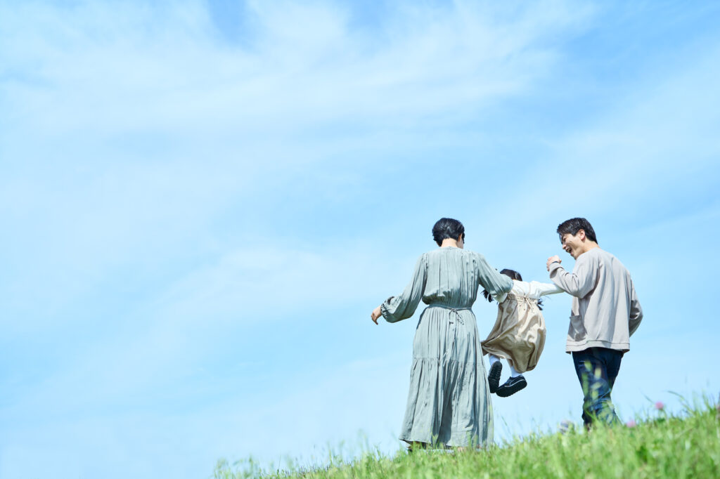 Two parents swing a small child between them while walking up a grassy hillside