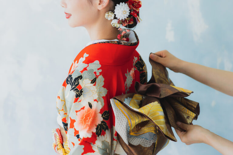 Woman being dressed in a kimono as someone ties her obi from behind