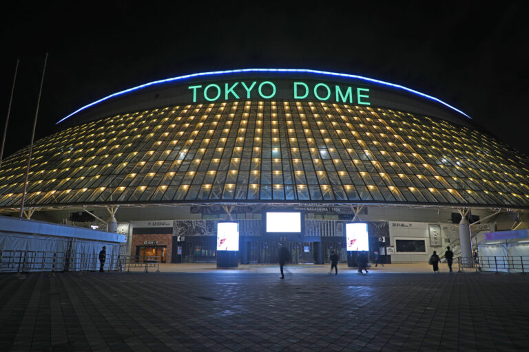 Tokyo Dome lit up at night, its illuminated sign glowing above a nearly empty entrance plaza