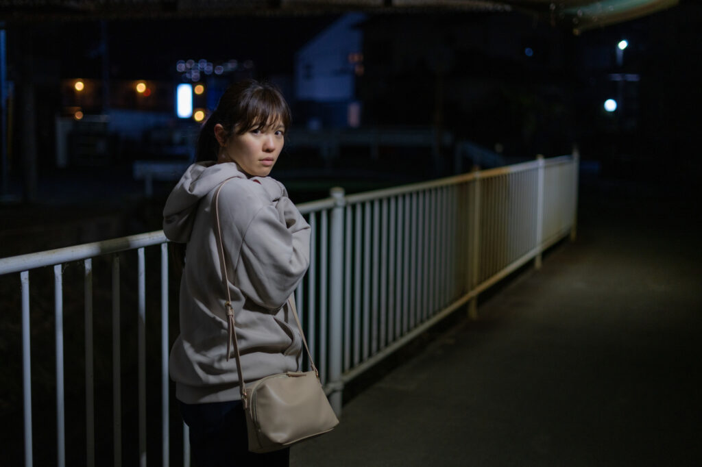 Young woman looking back anxiously on a pedestrian bridge at night