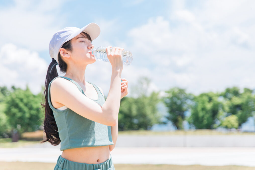 Young woman in a cap drinking from a water bottle outdoors on a sunny day.