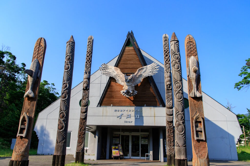 Carved wooden poles and an owl sculpture flank the entrance to the Ikor theater at Upopoy National Ainu Museum and Park