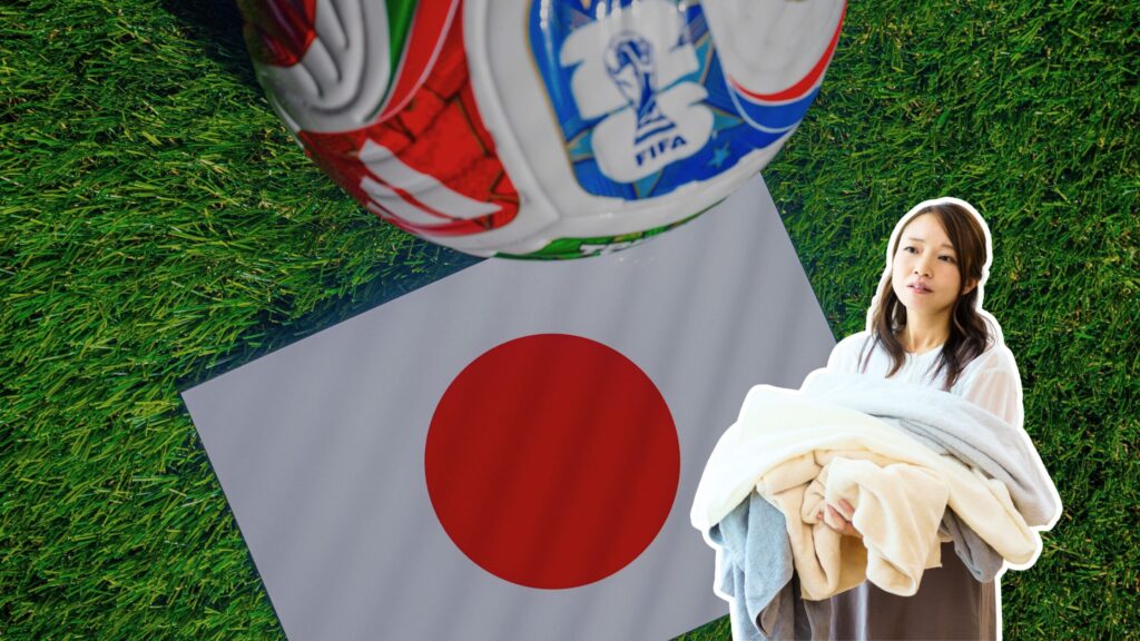 A FIFA World Cup soccer ball and a Japanese flag on grass, beside a woman holding a stack of folded laundry.
