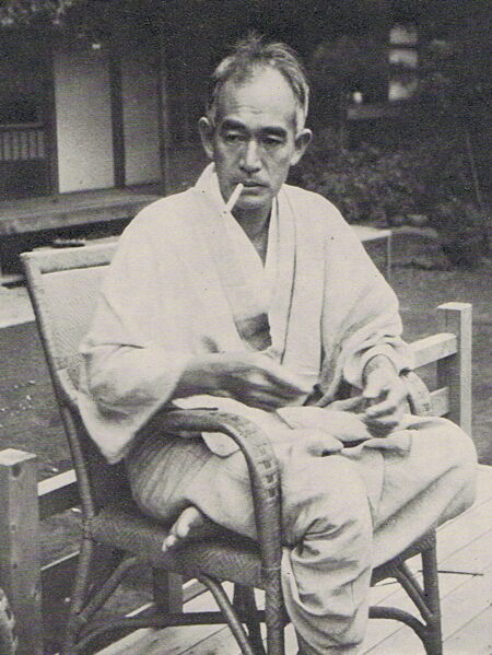 Novelist Shiga Naoya in a white kimono, smoking, seated in a wicker chair (black-and-white photo)