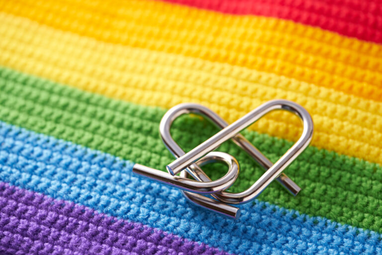 Two interlocking metal heart-shaped clips on a crocheted rainbow Pride flag
