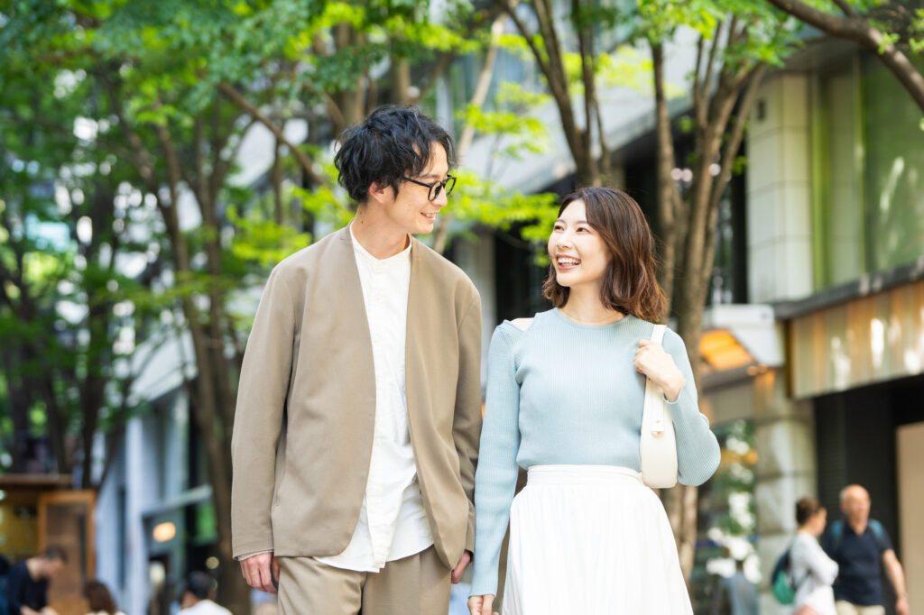 A young couple holding hands and smiling at each other on a tree-lined city street