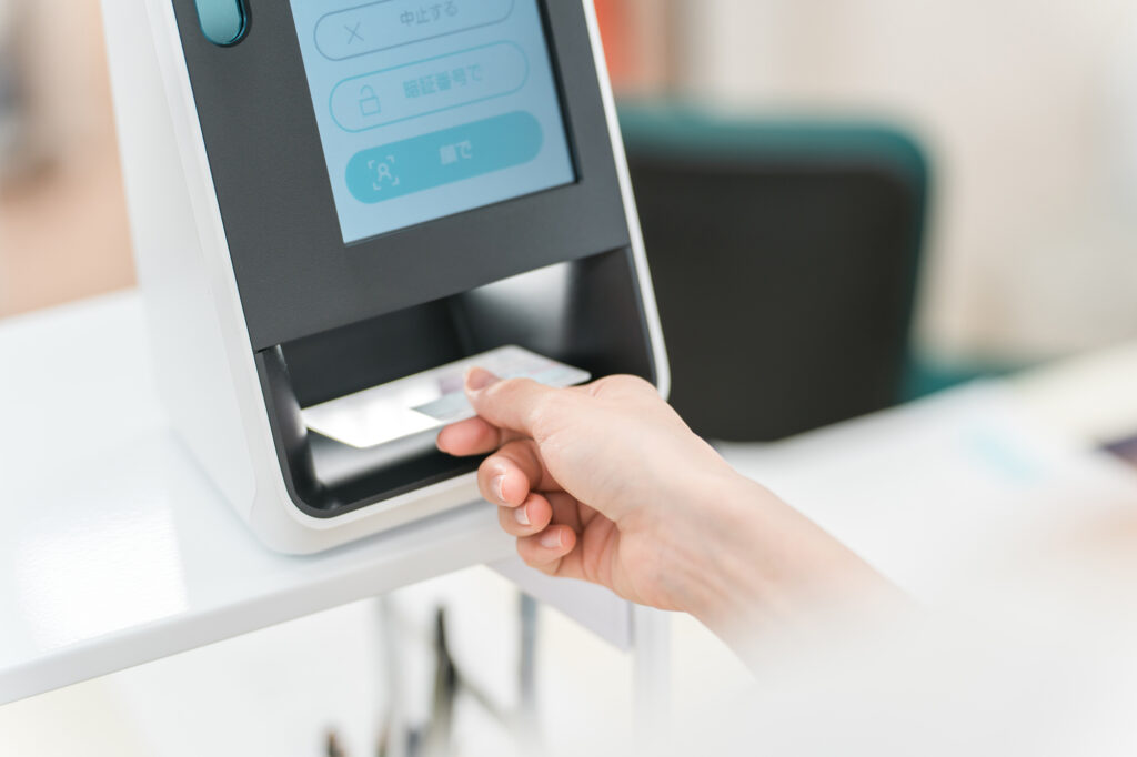 A hand inserting an ID card into a card-reader terminal with a Japanese-language touchscreen