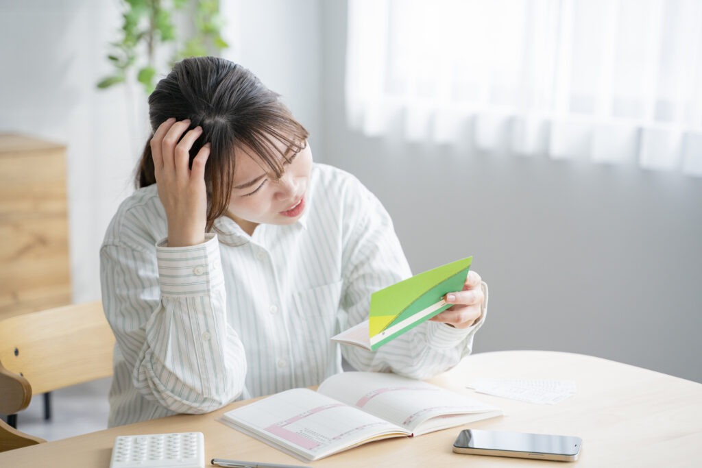 Woman holding her head while looking at a Japanese bank passbook at her desk