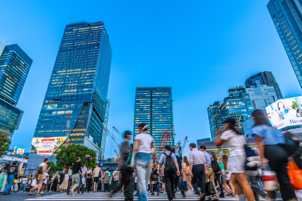 Pedestrians crossing a busy Shibuya intersection at dusk with skyscrapers in the background