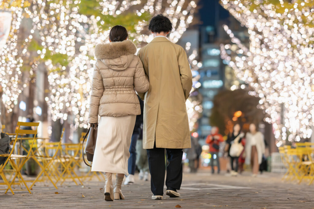 Couple seen from behind walking arm in arm down a street lined with winter illumination lights