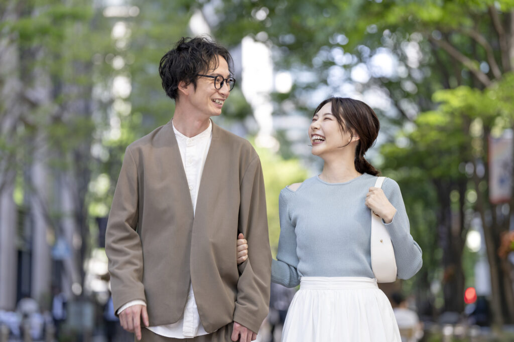 Young couple walking arm in arm and smiling at each other on a tree-lined city street
