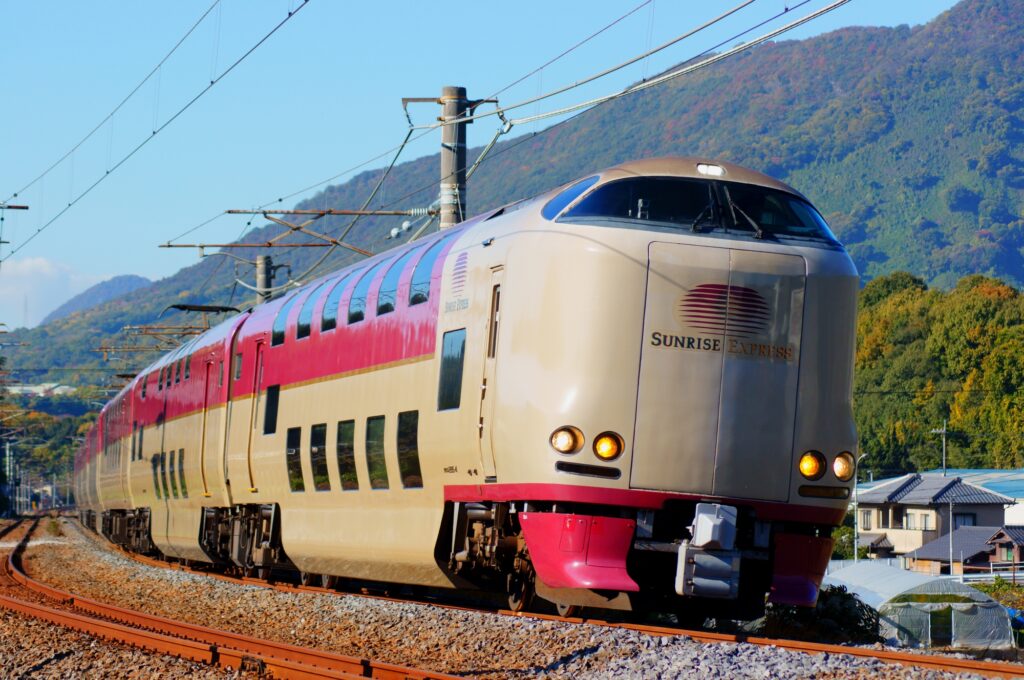 The cream-and-red Sunrise Express sleeper train rounding a curve past autumn hillsides