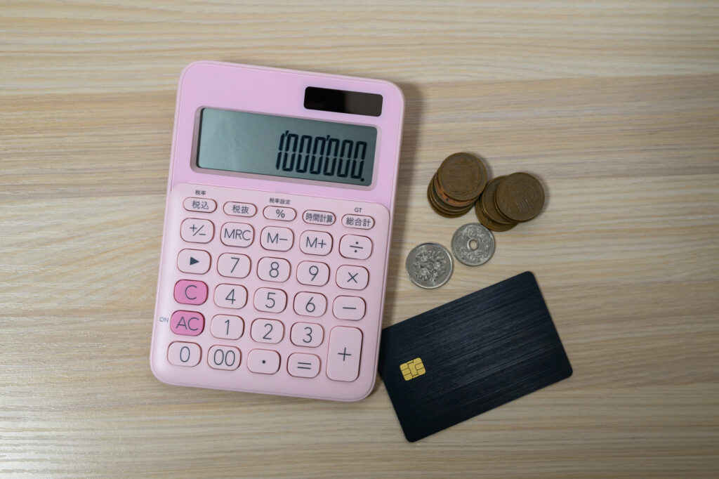 Pink calculator displaying one million yen beside Japanese coins and a credit card