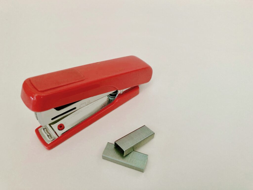 Red desktop stapler beside a strip of staples