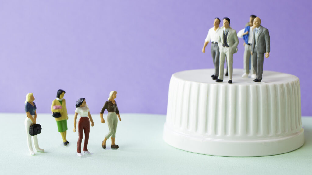 Miniature figurines of suited men on a raised pedestal above a group of women standing on the ground below