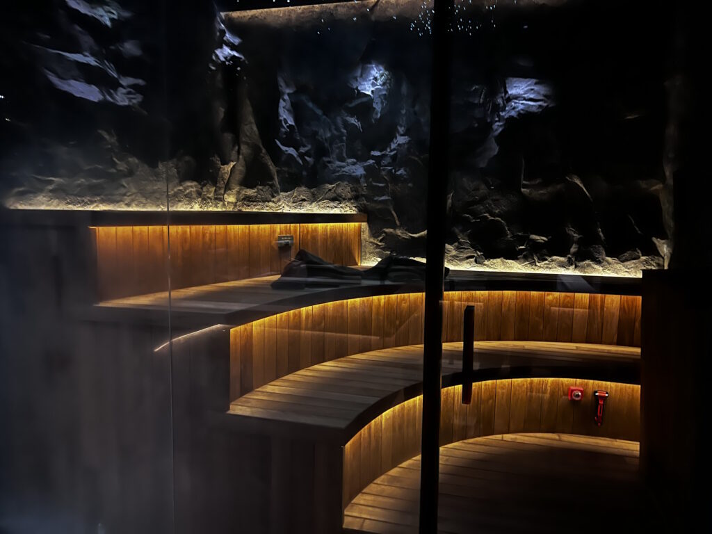 Private cave-themed sauna with curved tiered wooden benches and warm accent lighting behind a glass wall