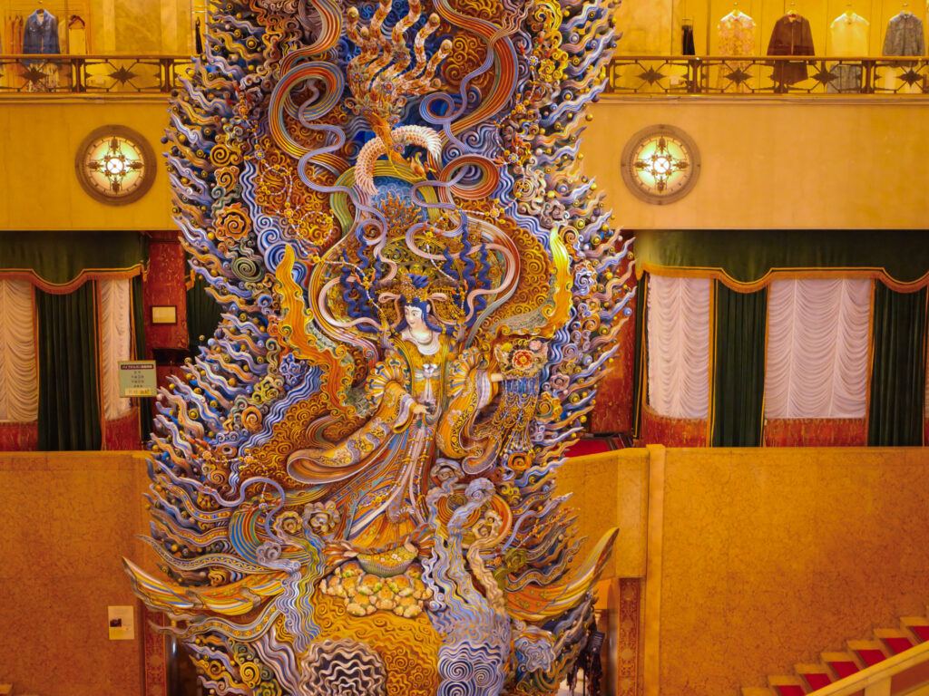 Angled view of the carved goddess among gilded swirling clouds, a phoenix above and her ornate pedestal below