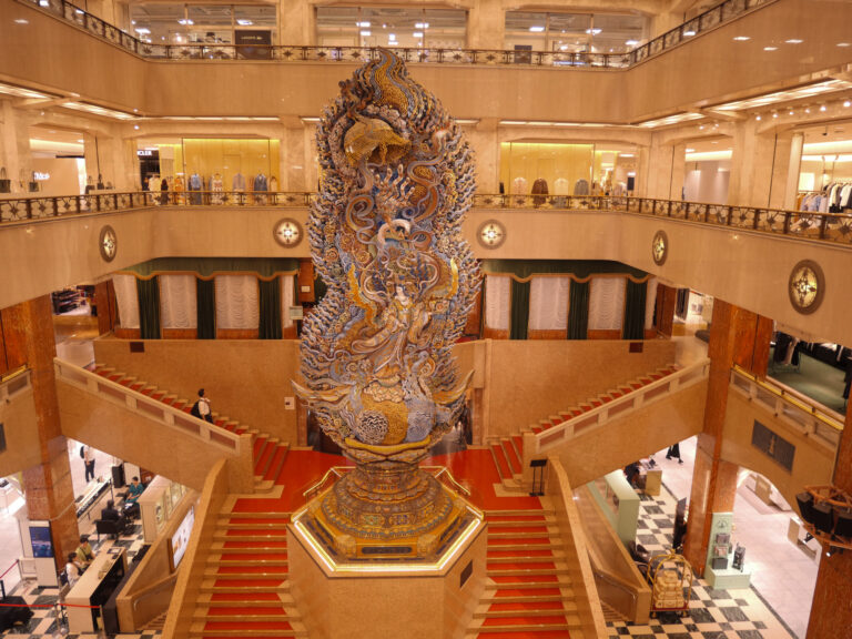 Mitsukoshi Nihonbashi's carved-wood goddess statue rising through the marble atrium above the red-carpeted grand staircase