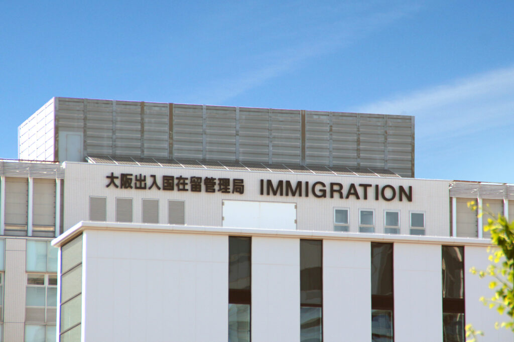 The Osaka Regional Immigration Bureau, its rooftop sign reading '大阪出入国在留管理局 IMMIGRATION,' under a blue sky.
