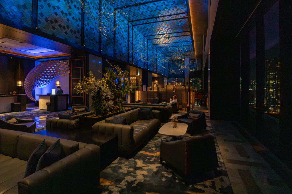Dimly lit upscale hotel lobby lounge at night with leather sofas and Tokyo city lights through the windows