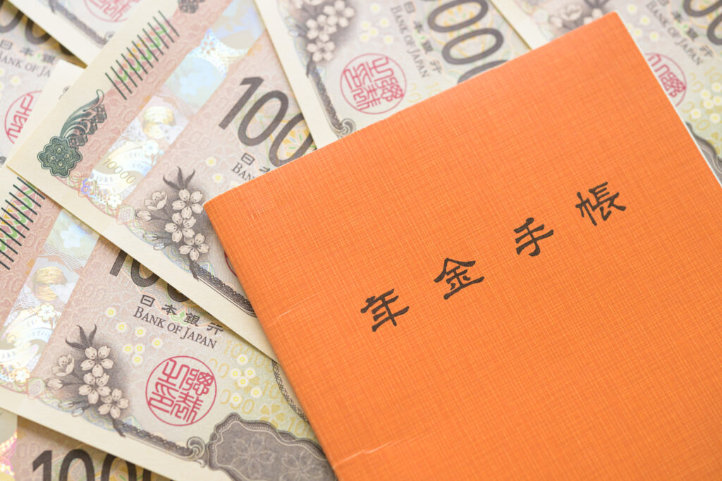 An orange Japanese pension handbook (年金手帳) resting on a spread of ¥10,000 banknotes.