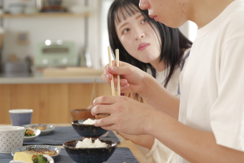 A young couple eat a rice-and-side-dish meal at home, the woman looking toward the man