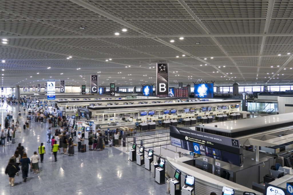 Travelers with luggage cross the wide check-in hall at Tokyo's Narita Airport, rows of counters under Star Alliance signage