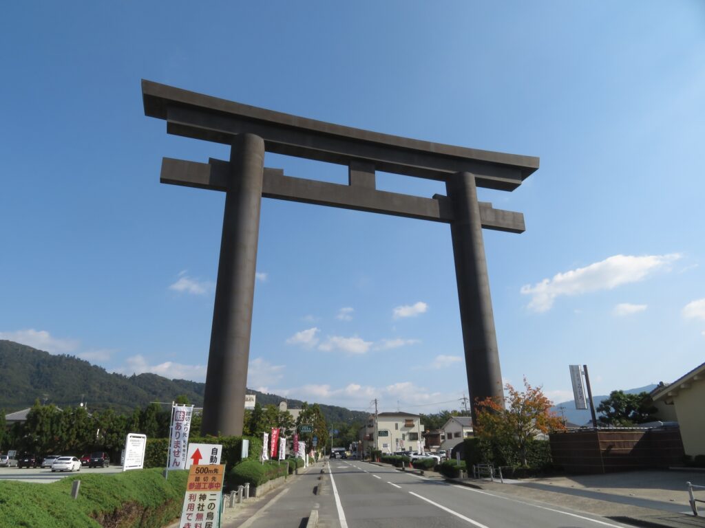 Ōmiwa Shrine's massive torii standing over a road, with the wooded slope of Mount Miwa beyond