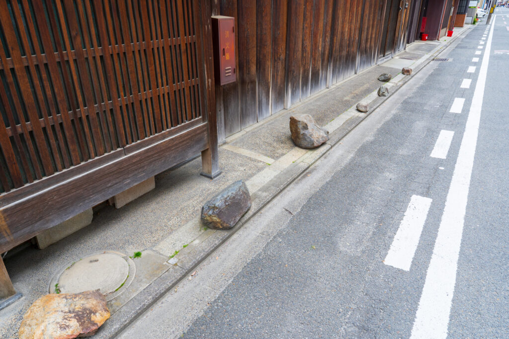 A row of ikezu-ishi stones lined along the base of a long wooden machiya wall on a narrow Japanese street.