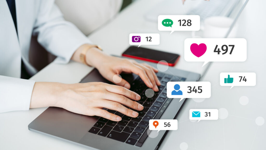 Hands typing on a laptop keyboard, surrounded by floating social media icons for likes, comments, followers and messages.