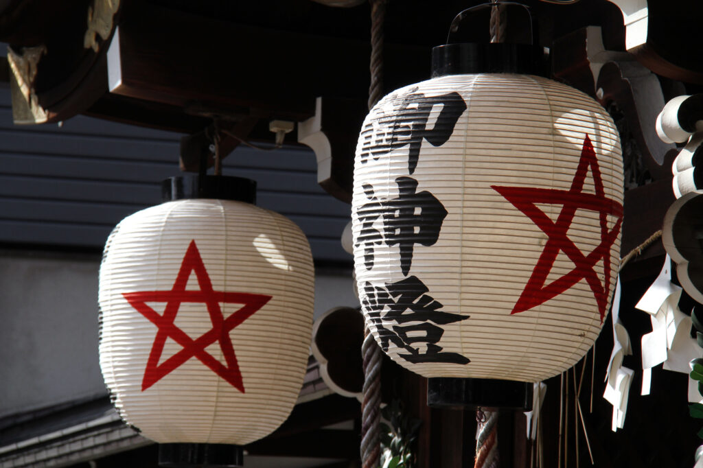 Two white paper shrine lanterns painted with red five-pointed Seimei stars and kanji reading sacred light