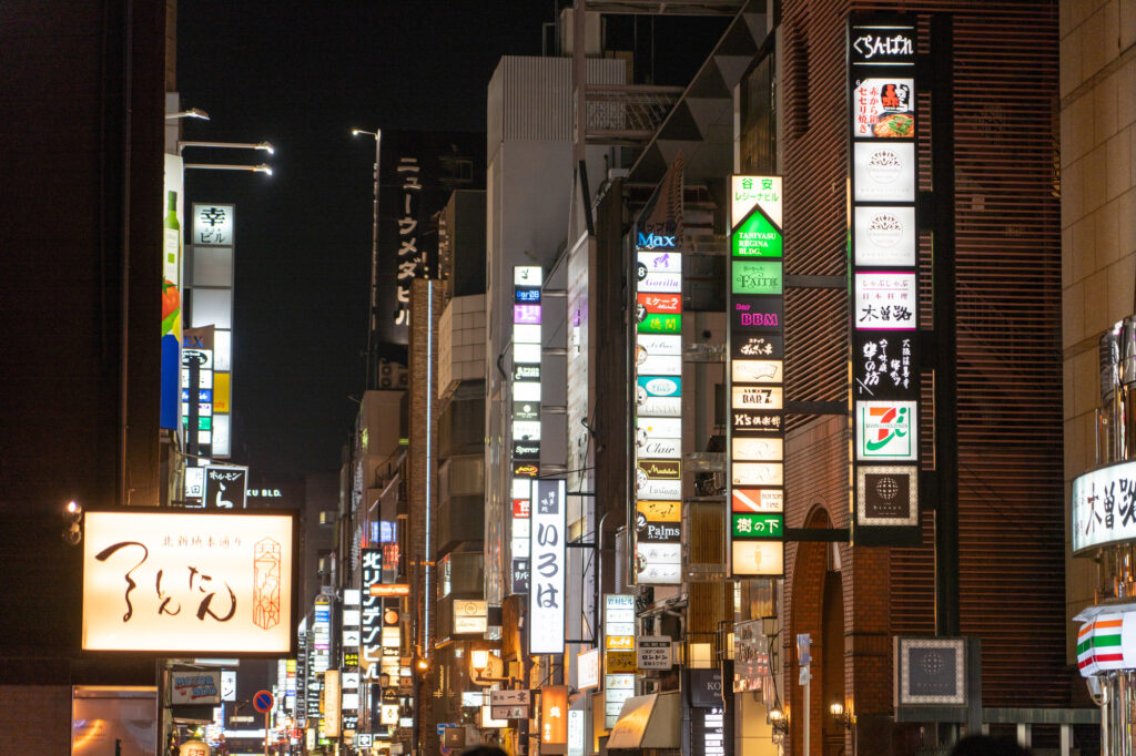 Illuminated vertical signs for bars and clubs crowd a nightlife street at night in Osaka's Kita-Shinchi district