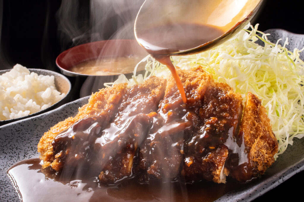 Dark miso sauce poured over a breaded pork cutlet (misokatsu) with shredded cabbage and rice, a Nagoya specialty