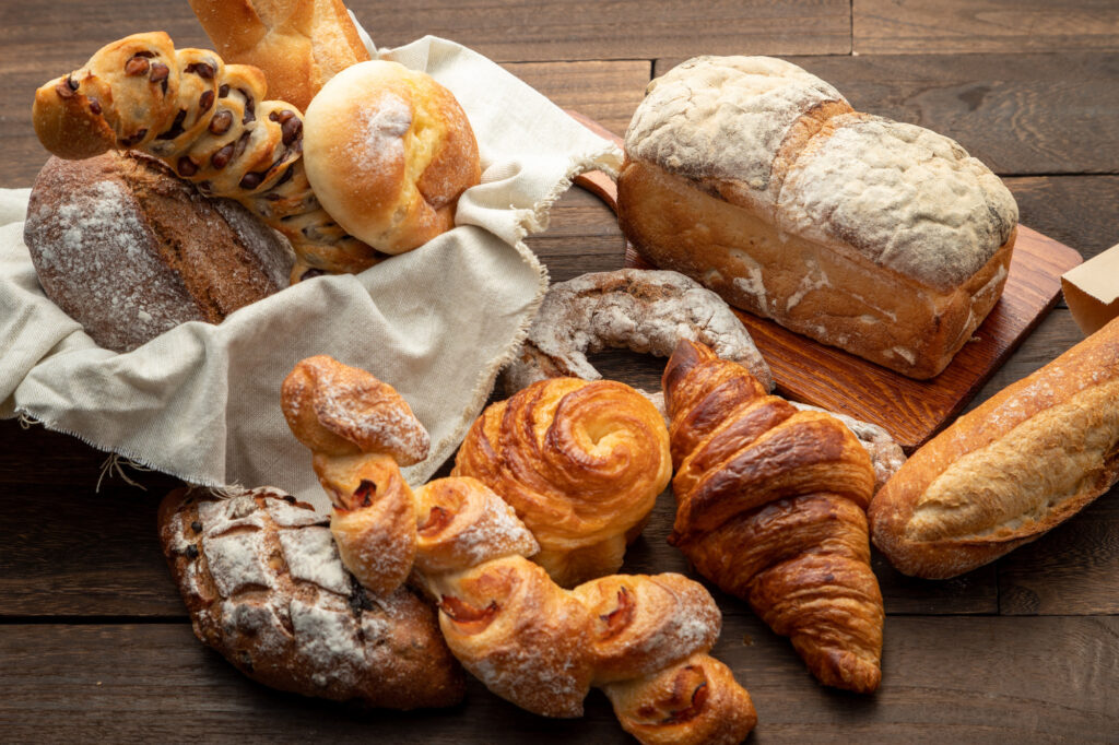 An assortment of breads, croissants, and pastries on a dark wooden table, some in a cloth-lined basket.