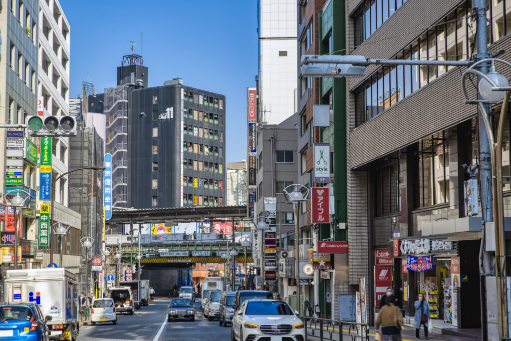 A busy Takadanobaba street lined with shops and signs, with a JR railway overpass in the background.